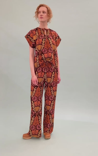 Woman in viscose pants and short sleeved top with large floral pattern in pink orange and yellow