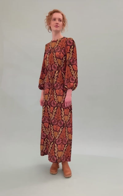 Woman in maxi dress in viscose twill with pink, yellow and orange flower pattern and puffed sleeves wearing boots