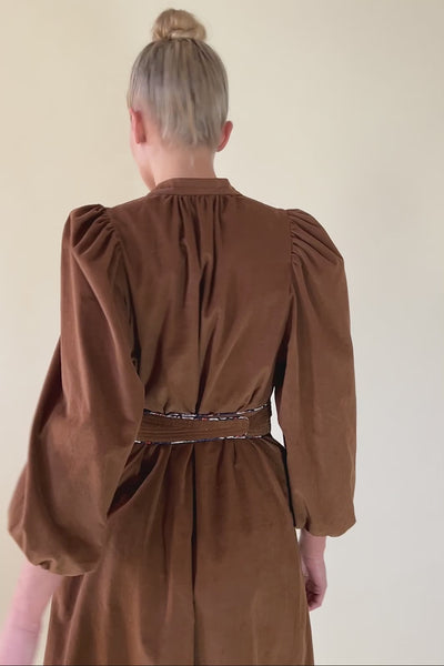 Woman in cognac brown baby corduroy dress with puff sleeves and matching belt