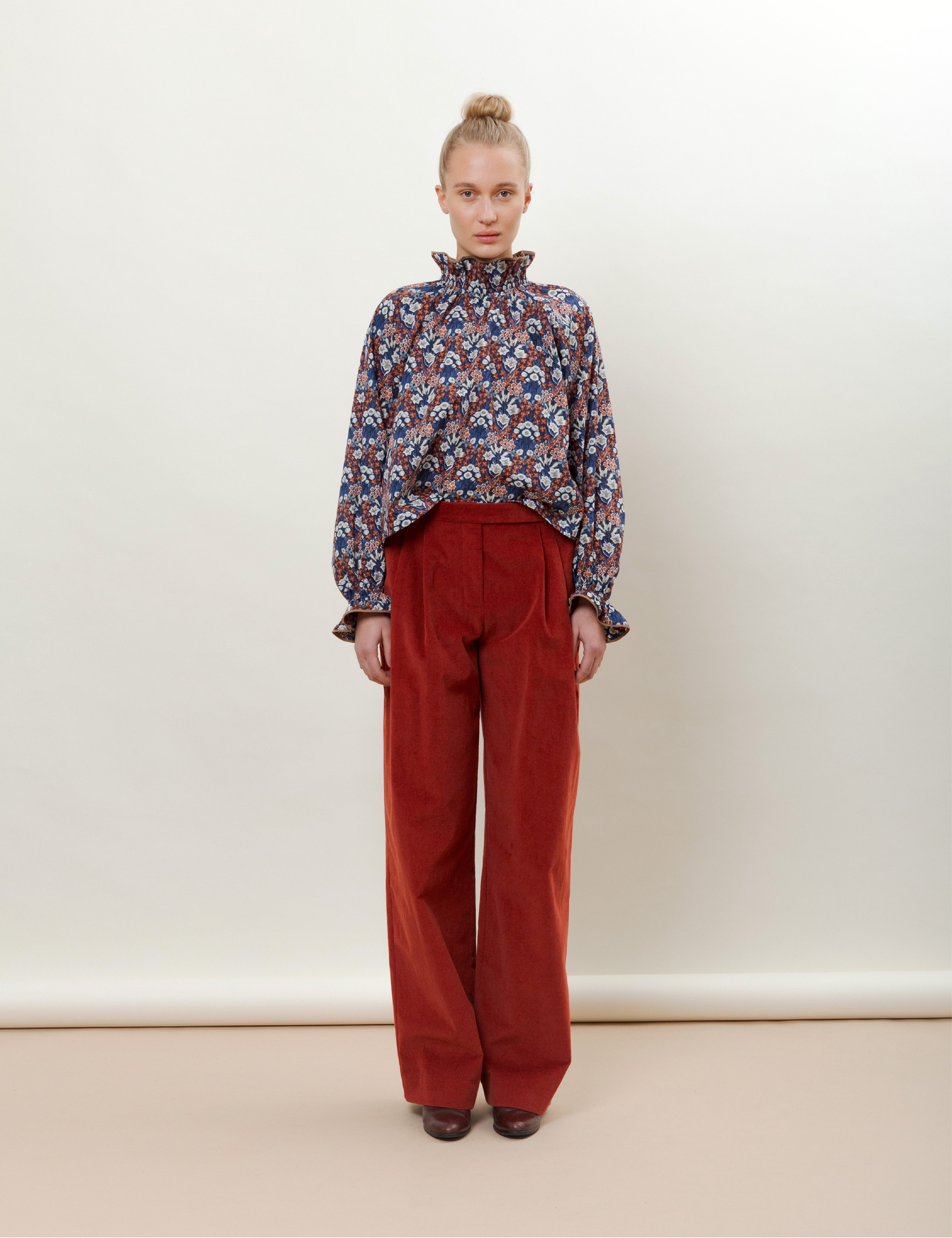 Woman in red wide corduroy trousers and blue red and white long sleeved flower patterned blouse with frills