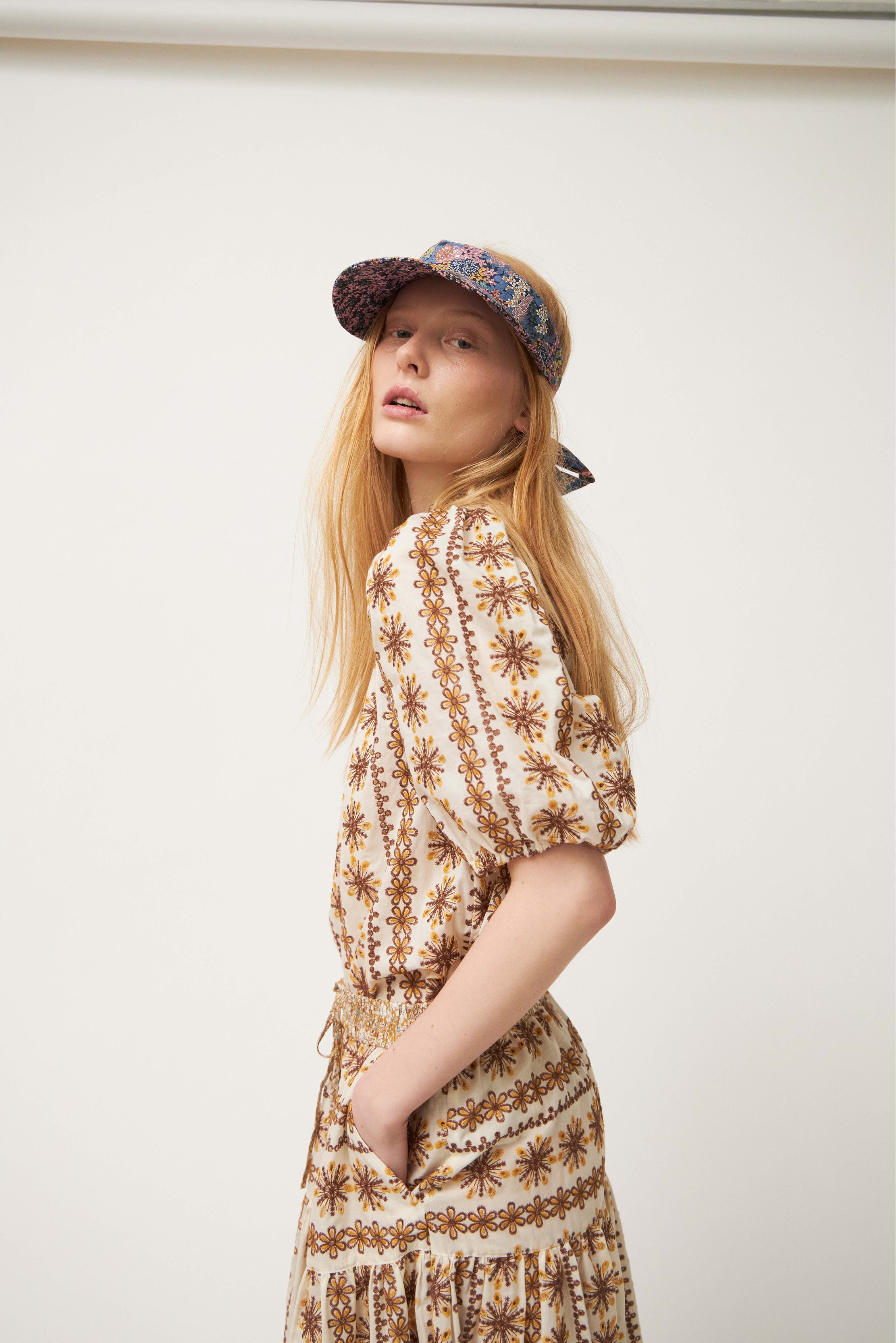 Woman i brown and white laced blouse and maxi skirt wearing Women's sun shade cap with multi colored flower pattern