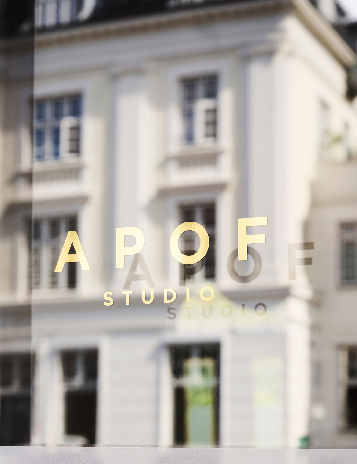 APOF Studio logo on a glass window with a light building facade reflected in the background.