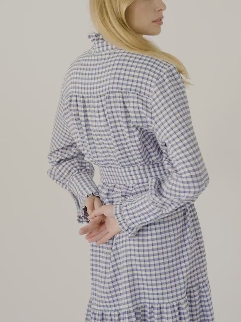 Woman in blue and white checked cotton dress with long sleeves, buttons, cuffs and collar with ruffles  and belt