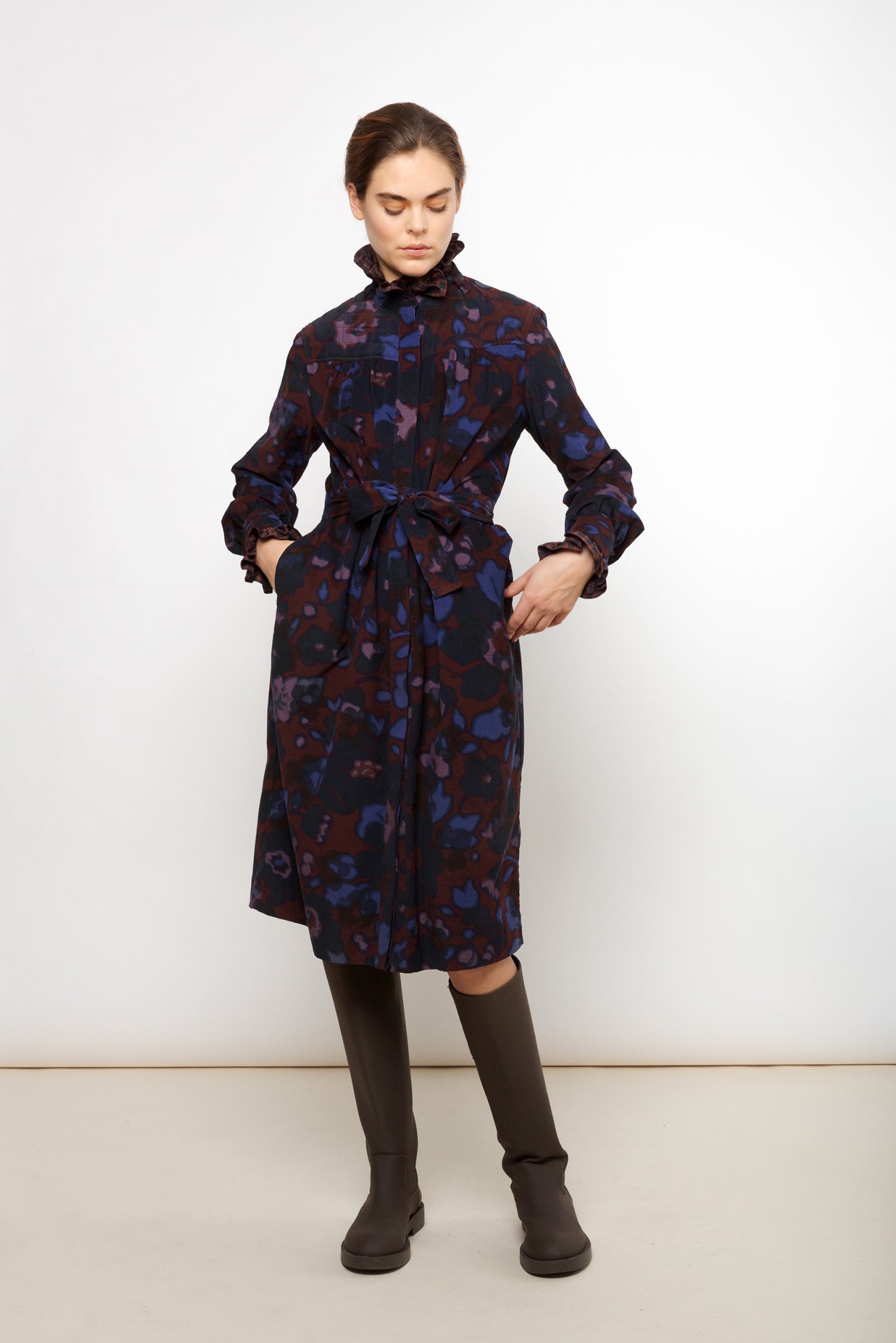 Woman in burgundy, pink and blue flower patterned dress with long sleeves and belt and brown boots